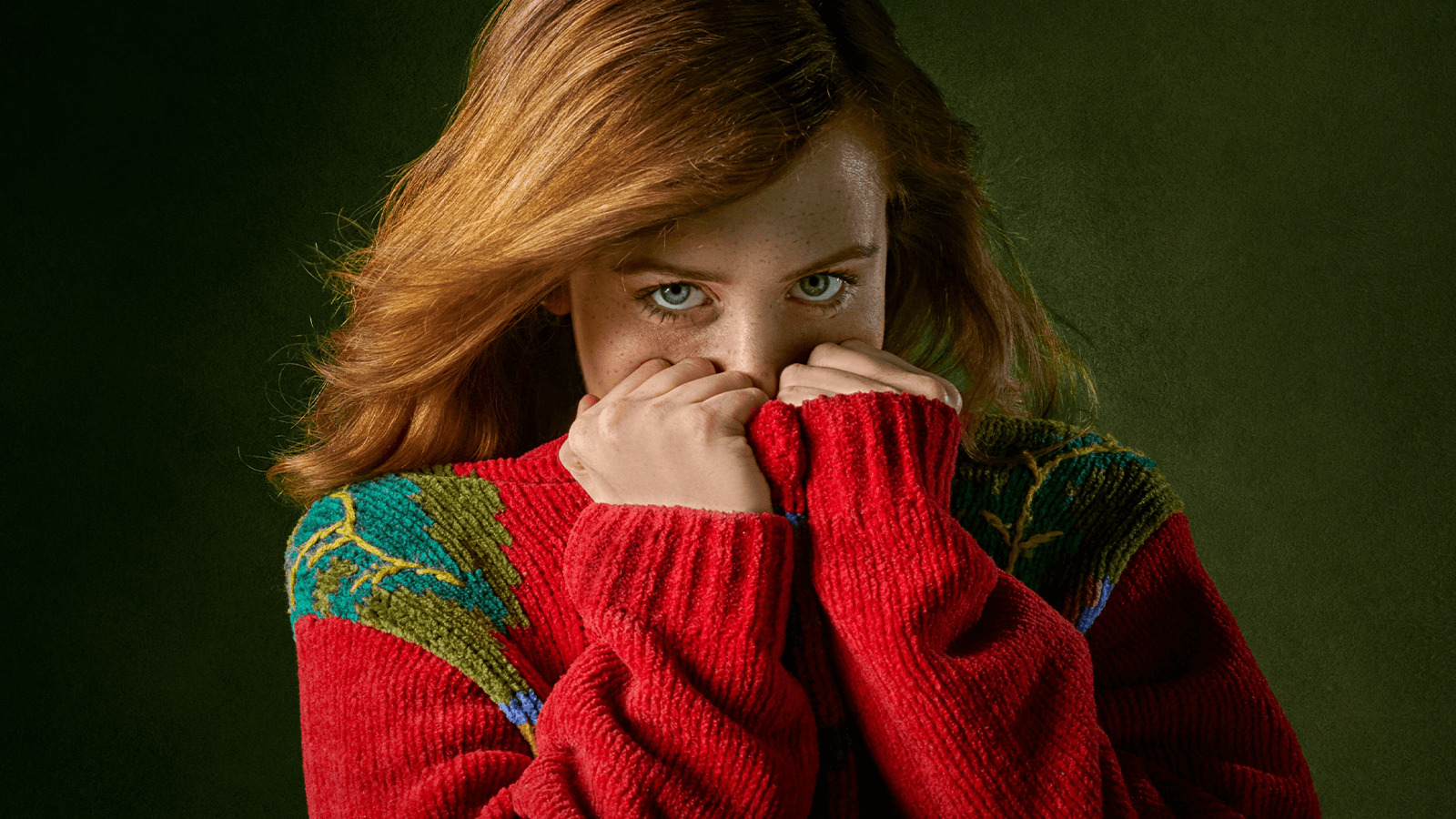 a woman in a red sweater covers her face with her hands.