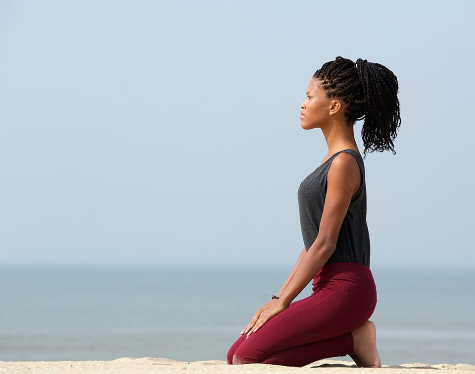 Woman kneeling at the beach in meditation