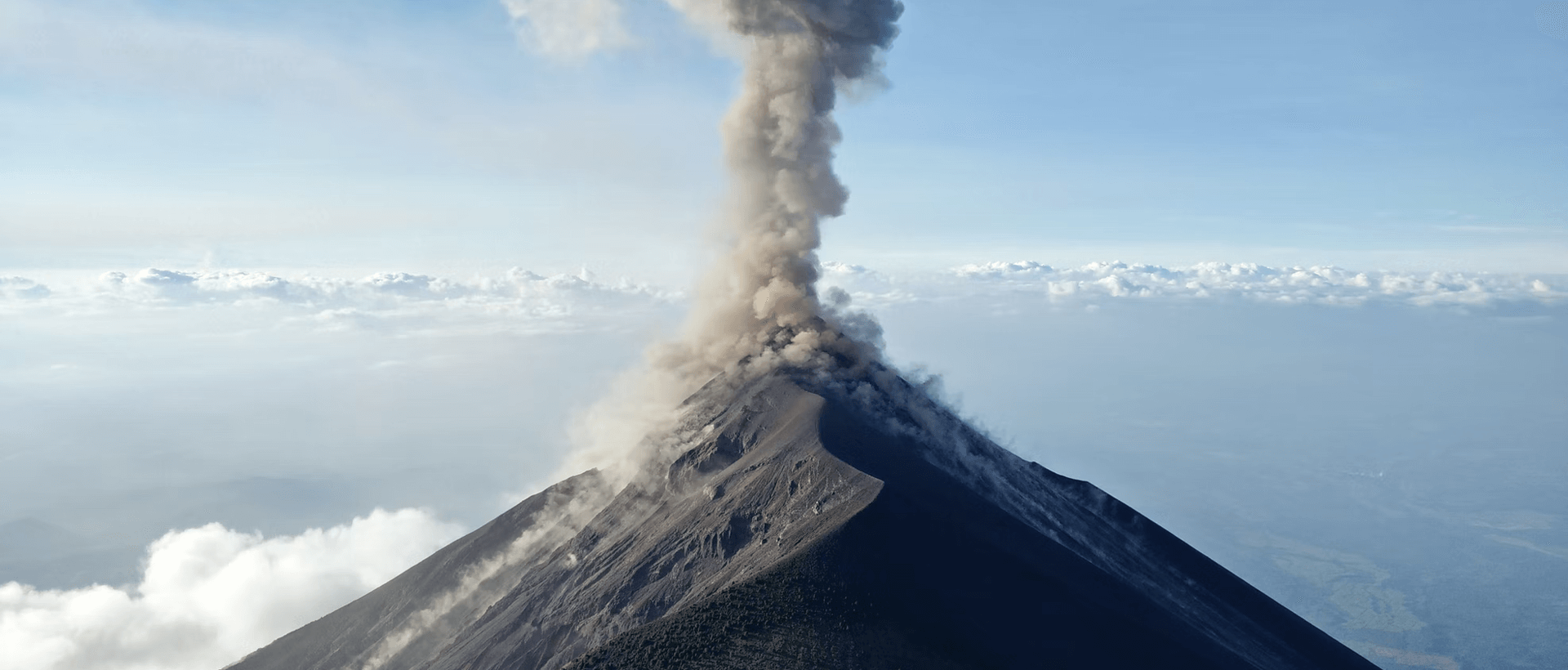 a plume of smoke billows from the top of a mountain.