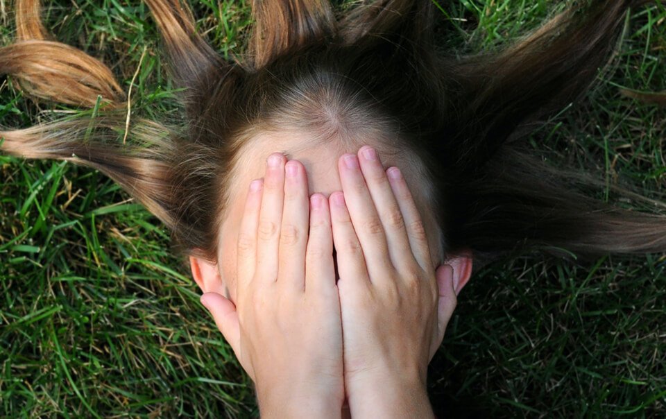 Femme couvrant le visage avec les mains et elle est allongée sur l'herbe remplie d'anxiété