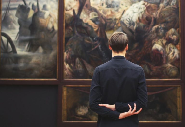 a man standing in front of paintings in a museum.