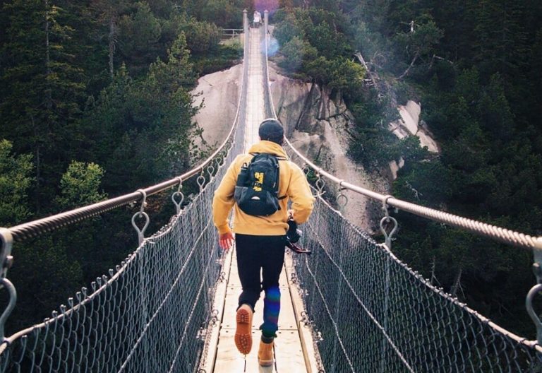 a man walking across a suspension bridge over a river.