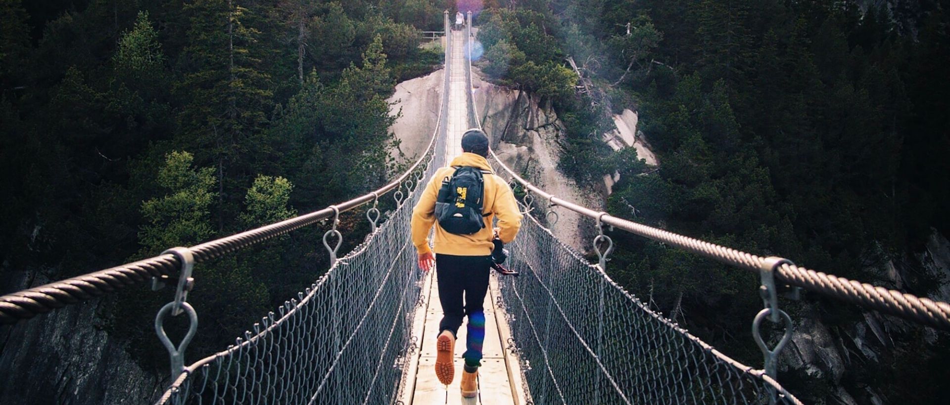 a man walking across a suspension bridge over a river.
