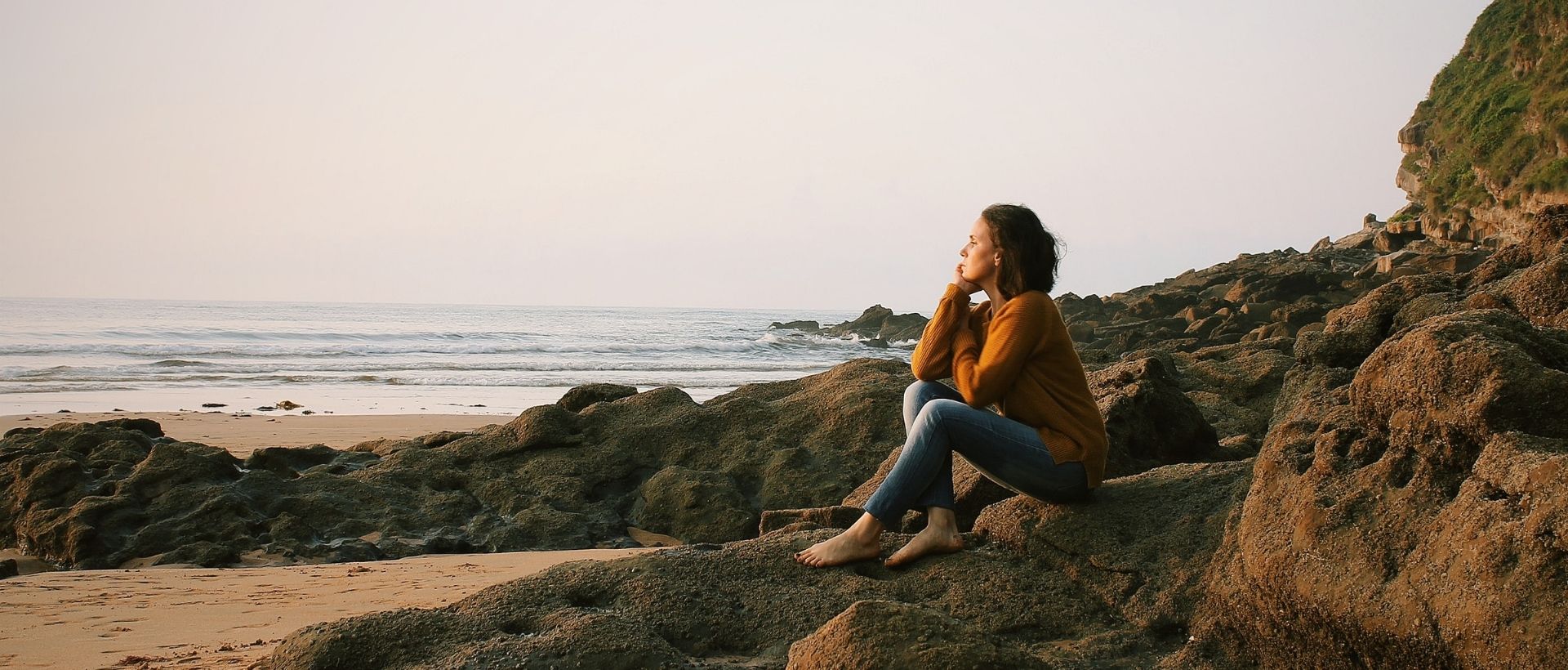 a woman sitting on a rock next to the ocean.