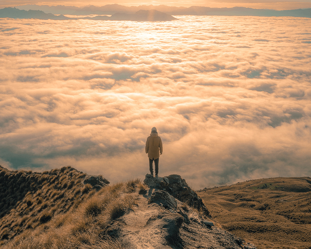 man on top of mountain overlooking clouds