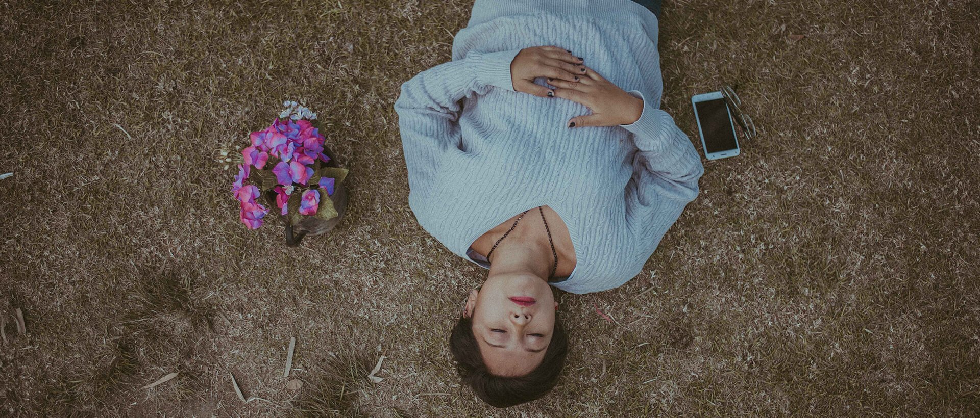 a man laying on the ground next to flowers and a cell phone.