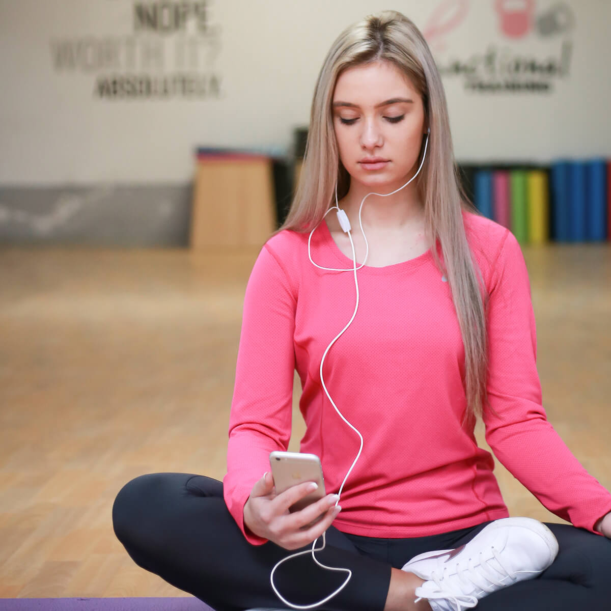 a woman sitting on a yoga mat listening to music.