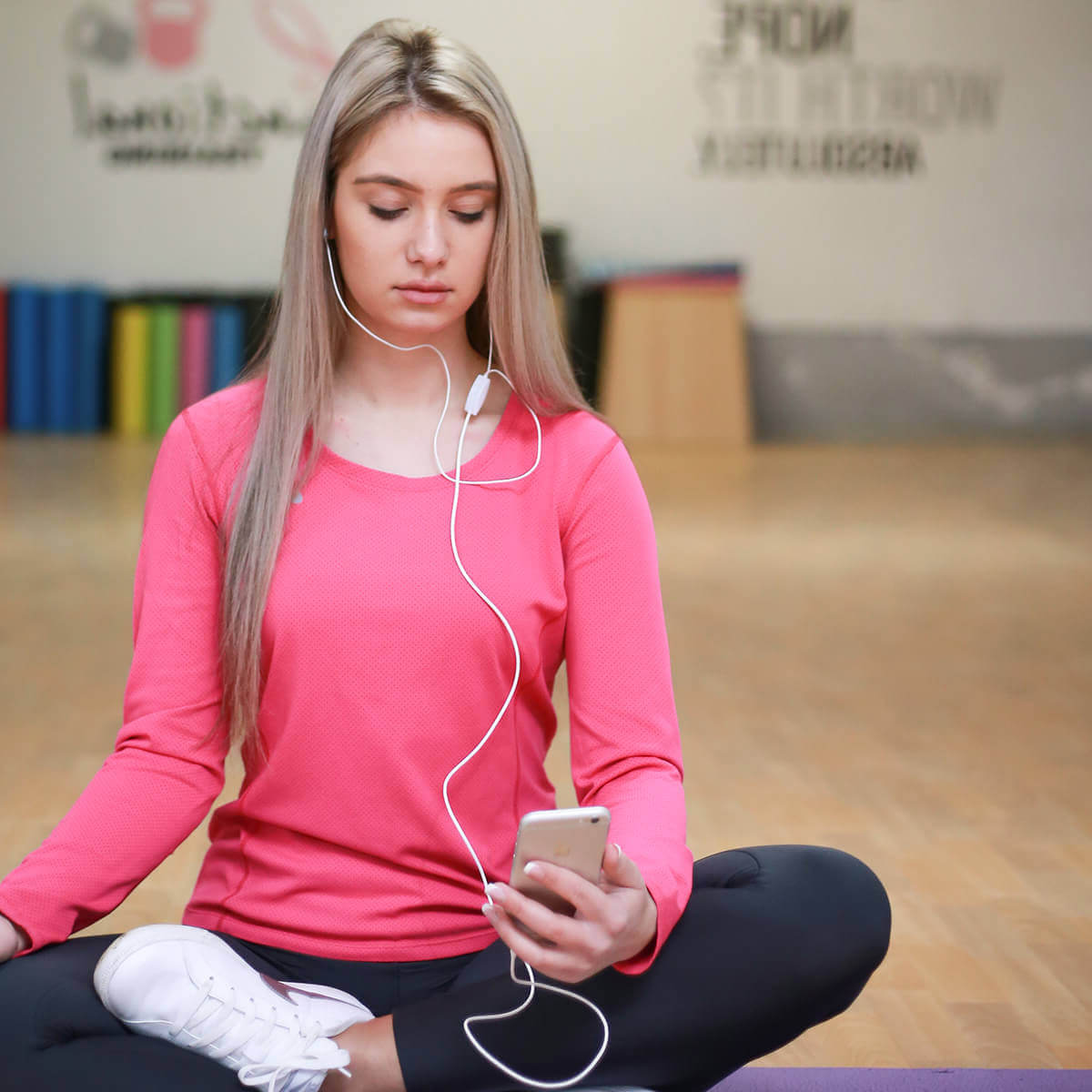 a woman sitting on a yoga mat listening to music.