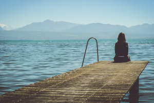 a woman sitting on a dock looking out at the water.