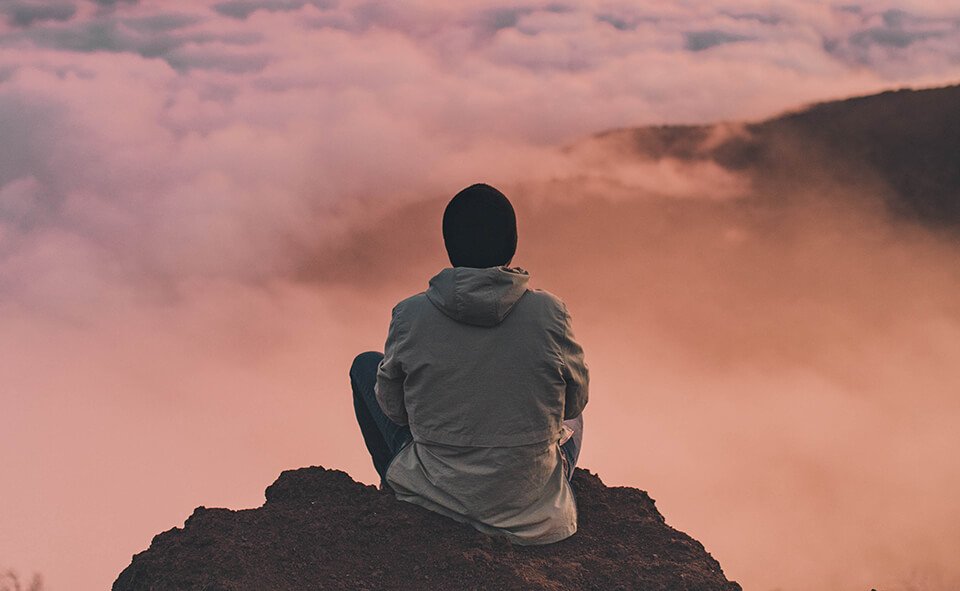 Man sitting on an edge of a rock, looking out to the clouds