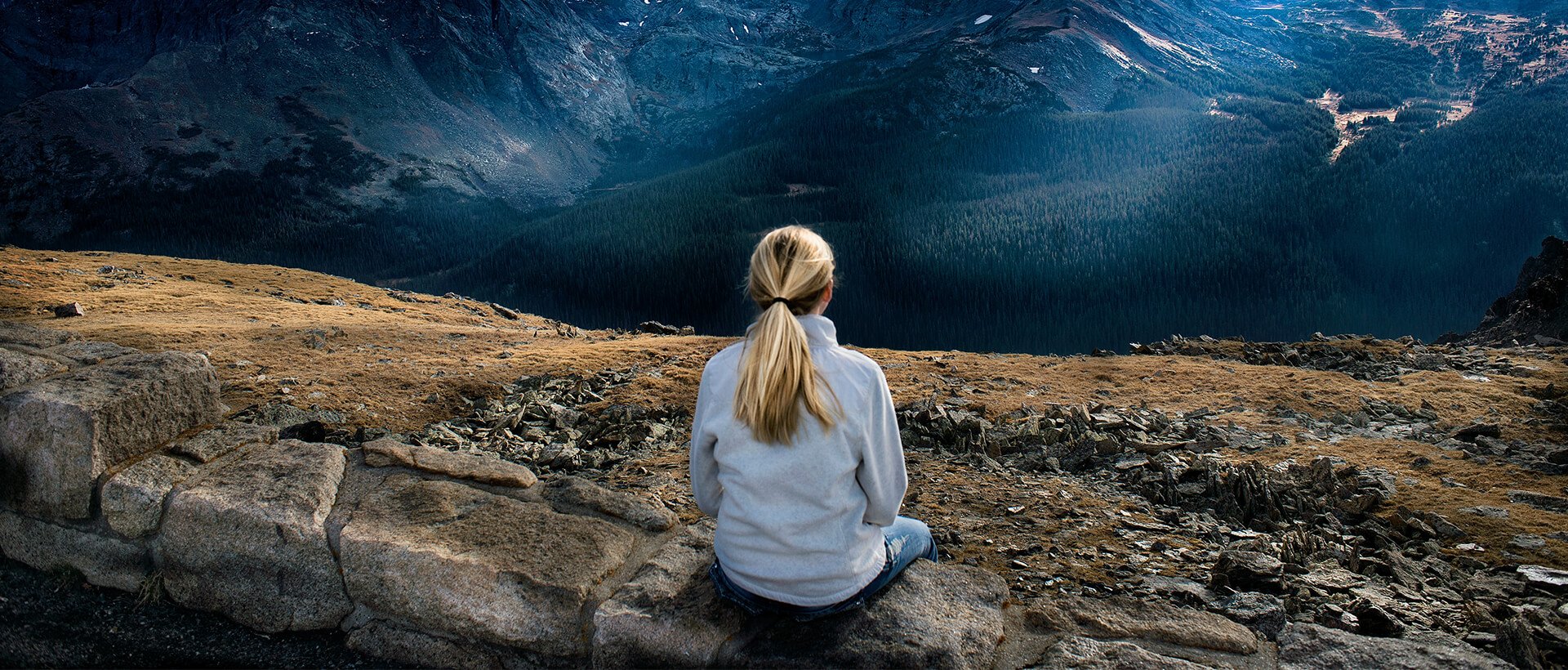 a woman sitting on top of a mountain overlooking a valley.
