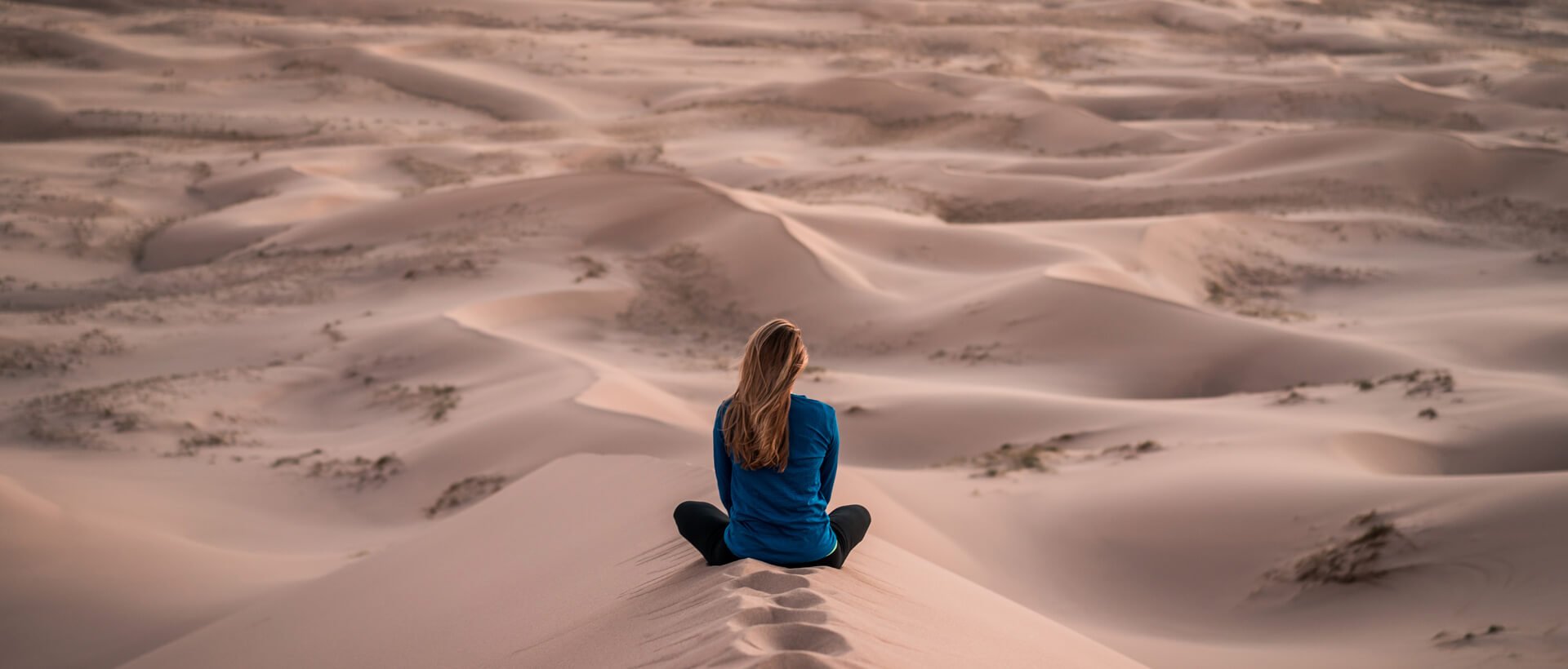 a woman sitting on top of a sand dune.