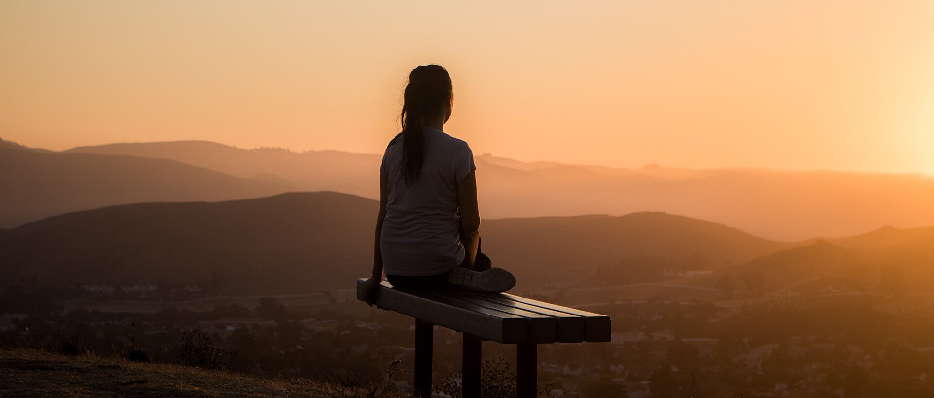 a woman sitting on a bench looking at the sunset.