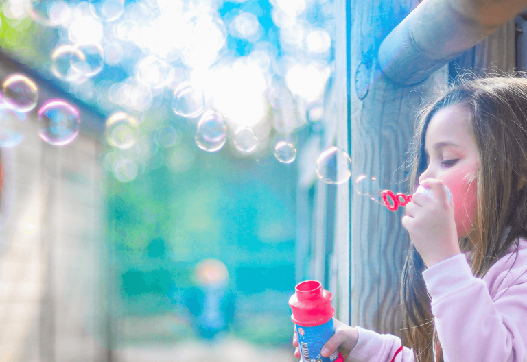 a little girl blowing bubbles out of a window.