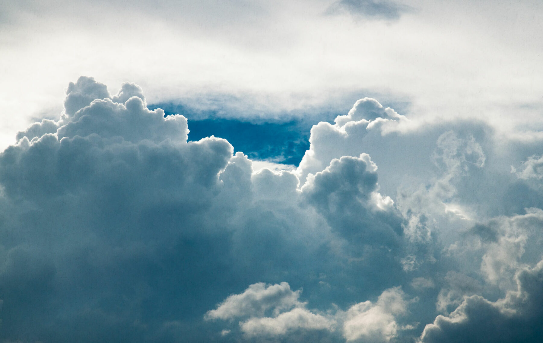 a plane flying through a cloudy blue sky.