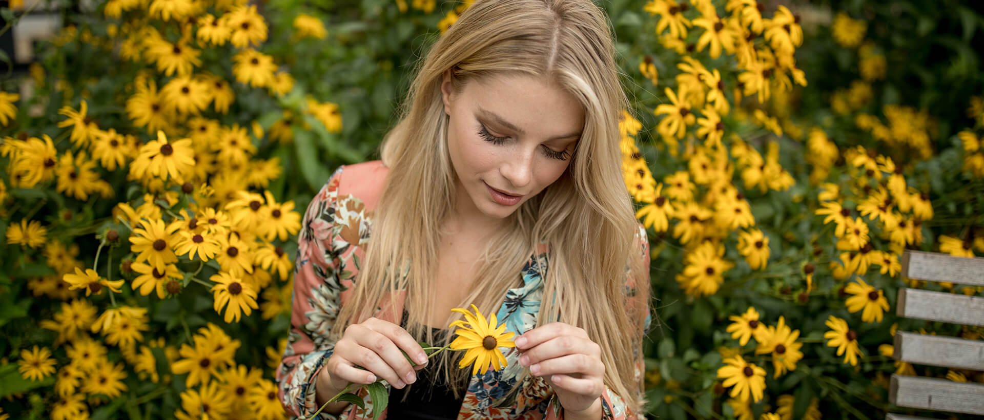 a woman holding a yellow flower in front of a bunch of yellow flowers.