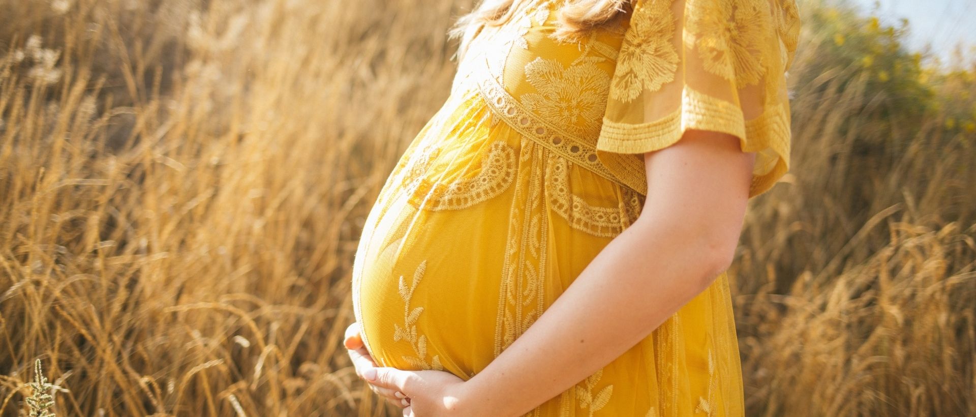 a pregnant woman in a yellow dress standing in a field.