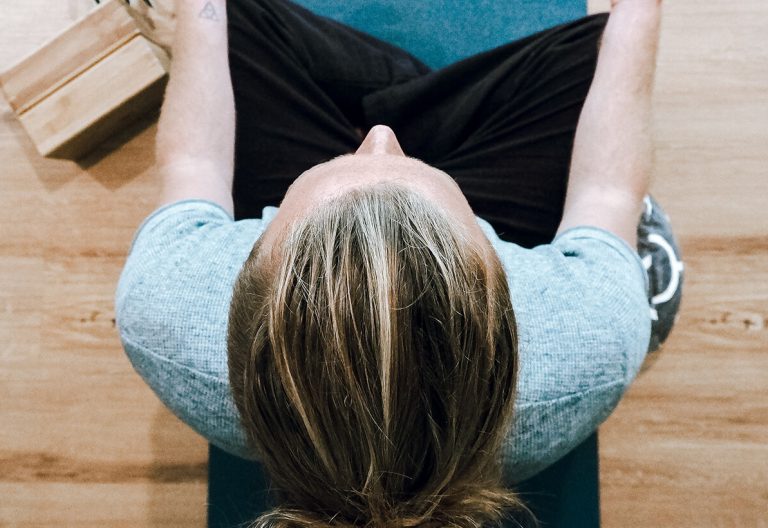 a woman sitting on a yoga mat with her hands behind her head.