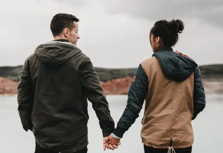 a man and a woman holding hands while standing next to a lake.