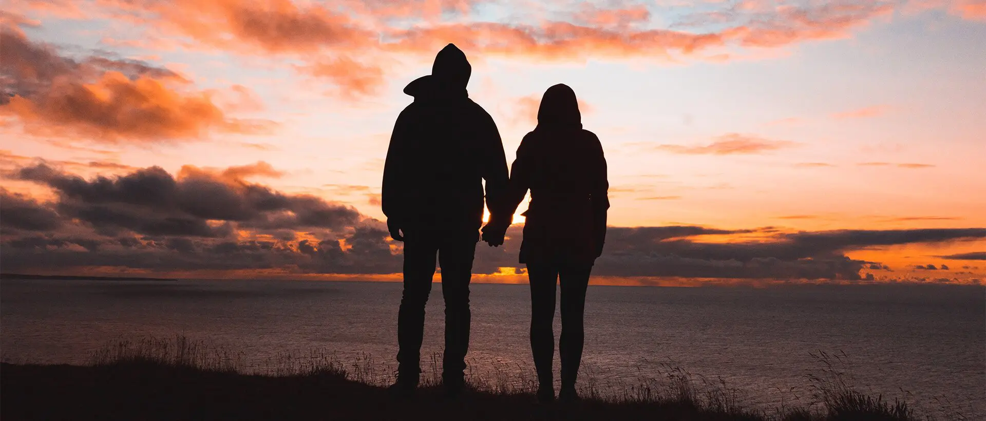 a man and a woman holding hands as the sun sets.