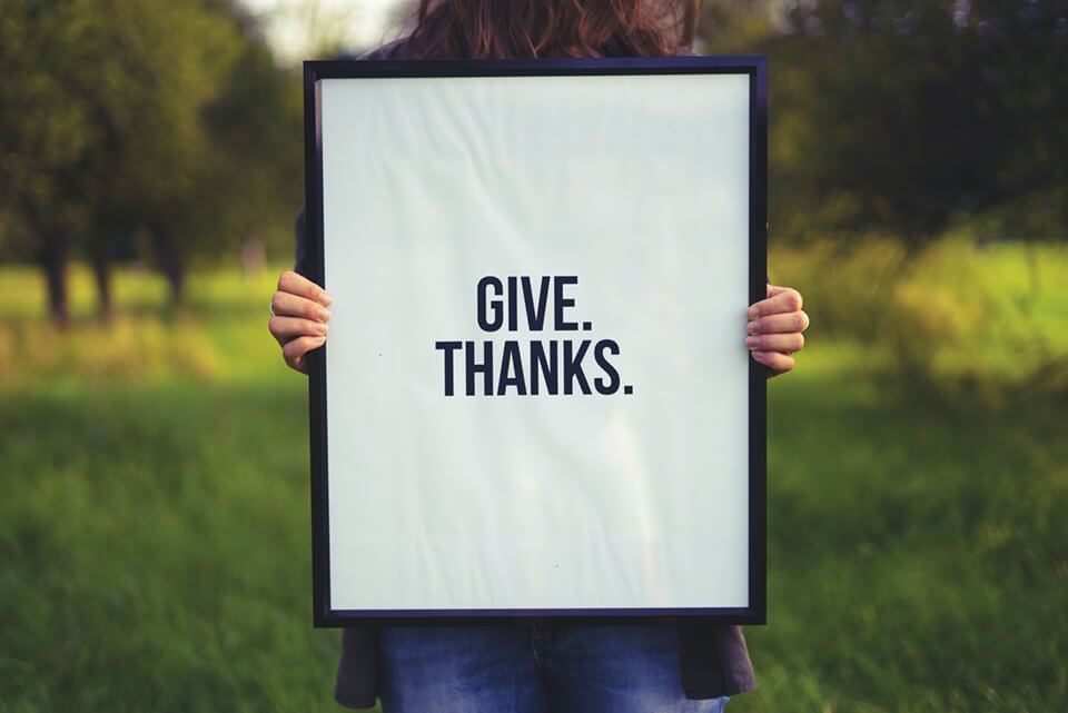 Woman holding up portrait with the word "Give thanks." on it.
