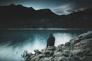 a man sitting on a rock looking at the water.
