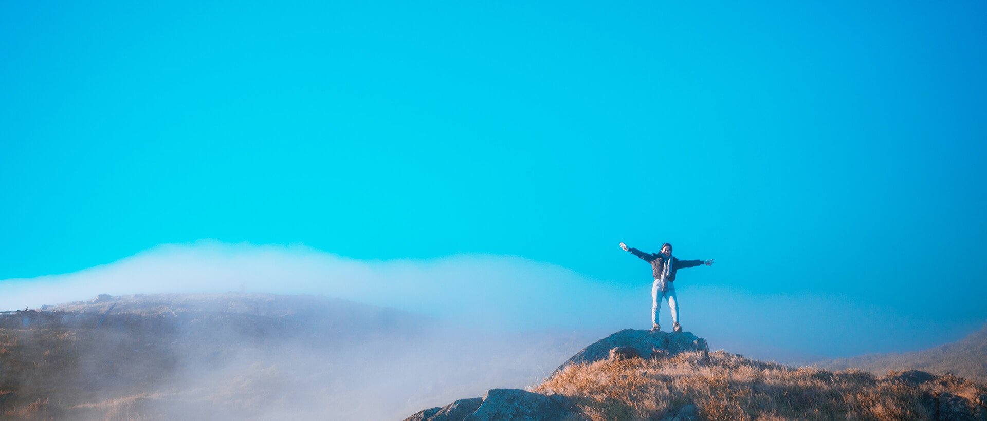 a person standing on top of a mountain with their arms outstretched.