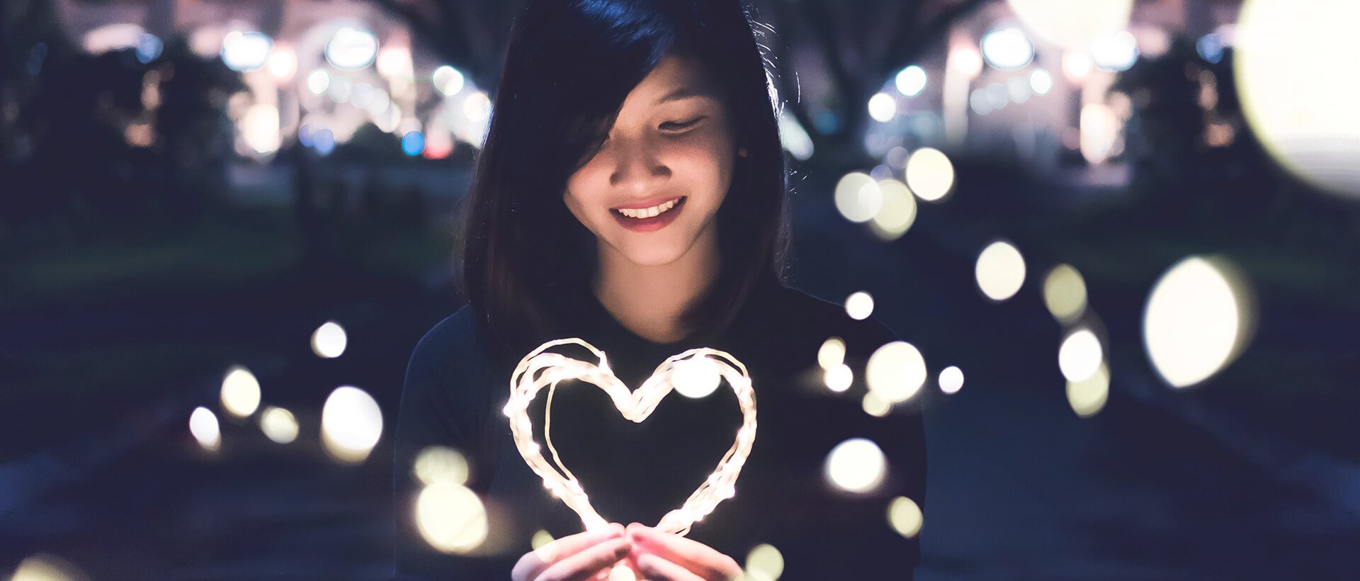 a woman holding a lit up heart in her hands.