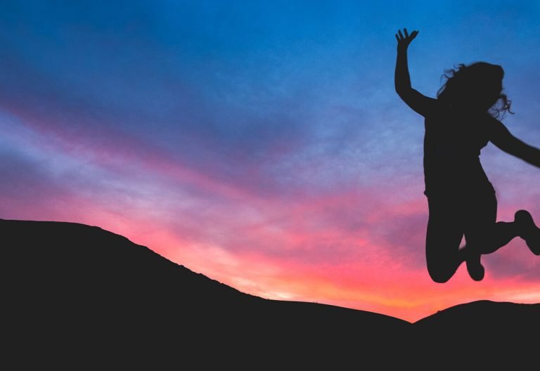 a woman jumping in the air at sunset.