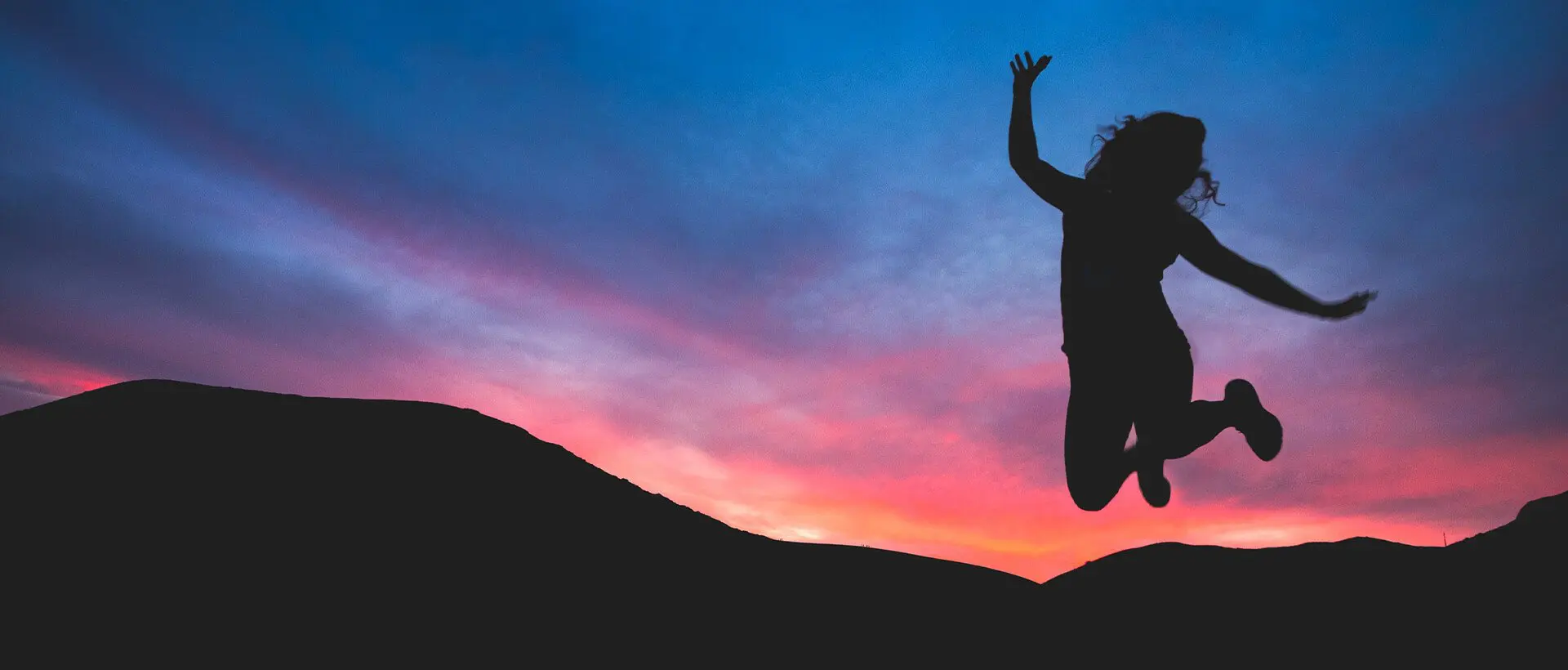 a woman jumping in the air at sunset.