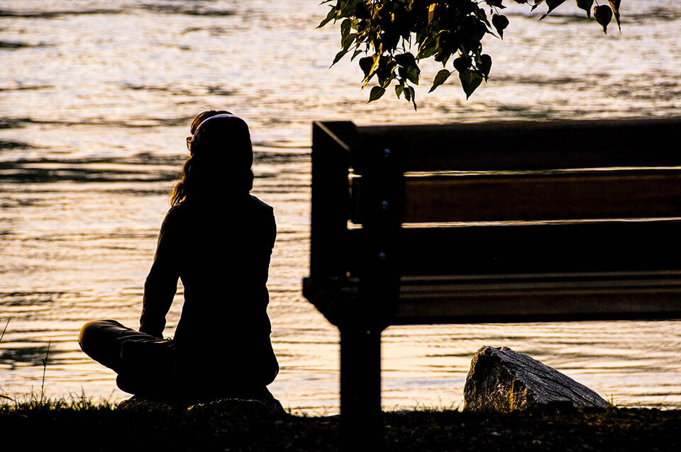 Woman sitting at park meditating near the water