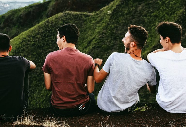 a group of young men sitting on top of a lush green hillside.