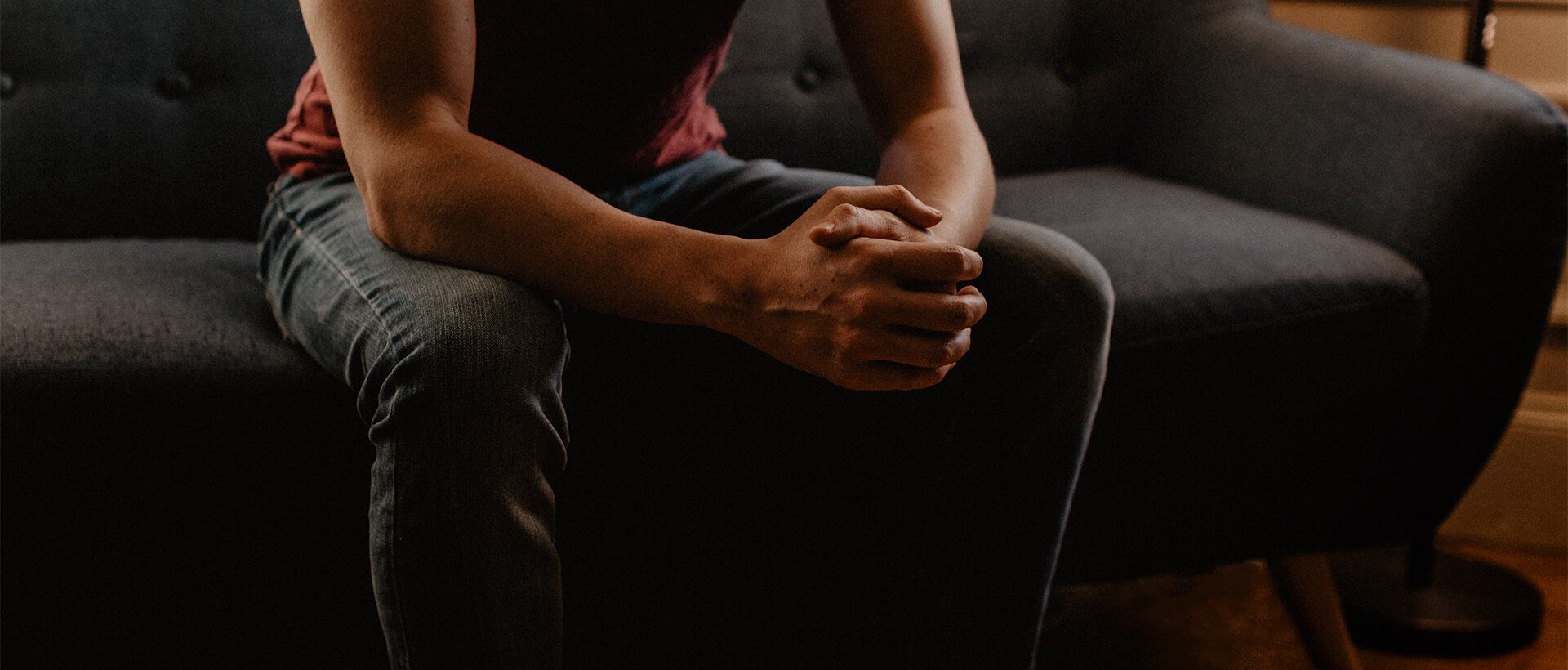 a person sitting on a couch with their hands clasped.
