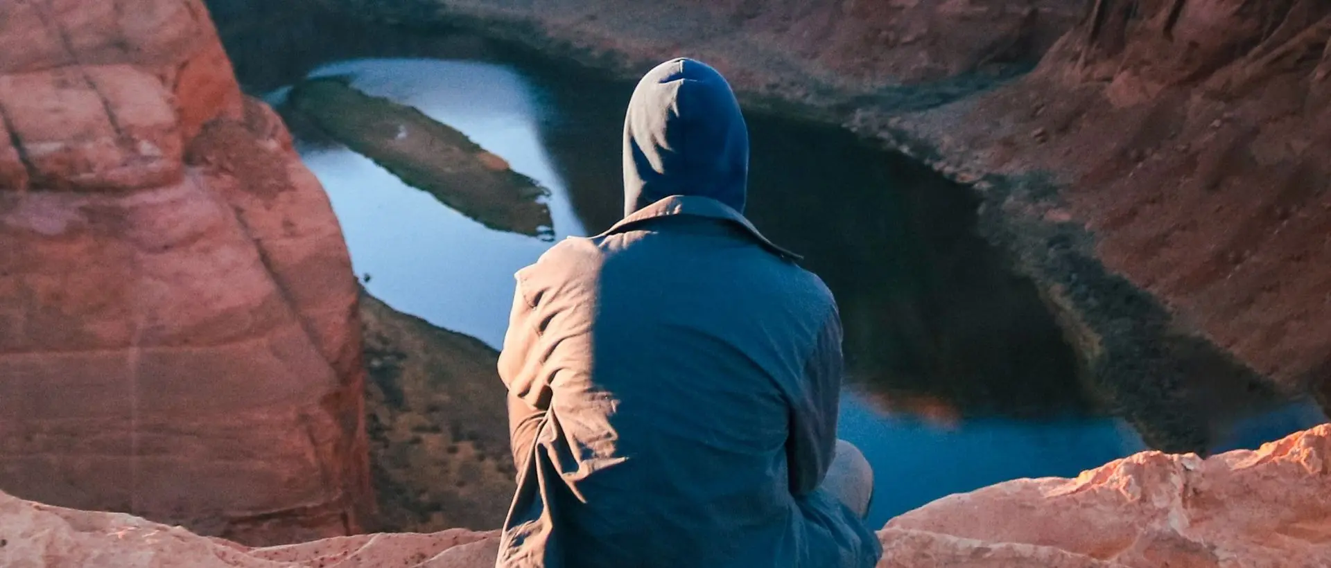 a person sitting on a rock looking at a lake.