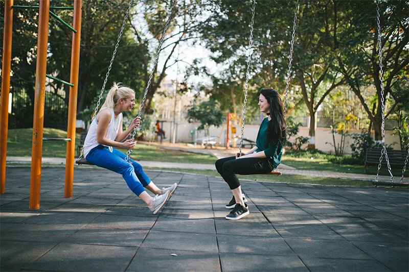 Two women talking to one another on a swing set