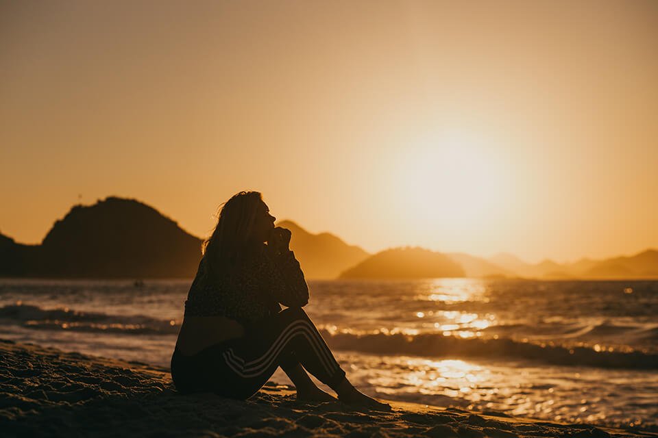 Woman sitting on beach lost in thought