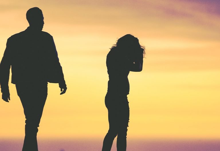 a man and a woman standing on a beach at sunset.