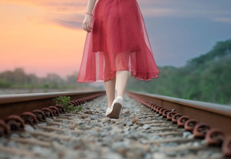 a woman in a red dress walking on a train track.