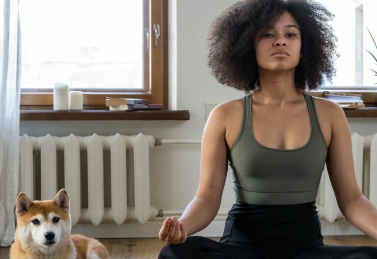 a woman sitting in a yoga pose with a dog.